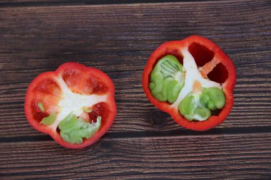 Dilimlenmiş kırmızı dolma biber. Ahşap bir masada yeşil biber yetişir.