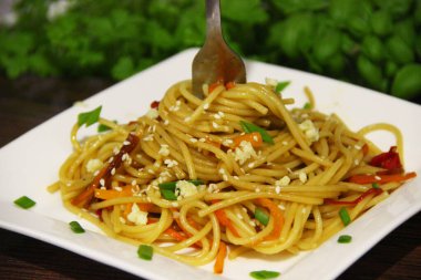 Sebze ve soya soslu spagetti, sarımsak ve susam serpilmiş, çatala sarılmış, beyaz kare bir tabakta.