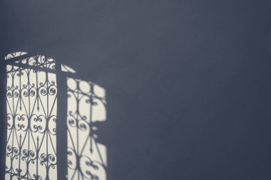 Demirden dövülmüş çit kapısı sabah ışığında duvarda kontrastlı gölge. Üzücü soğuk gri renkler. Metin için boş kopya alanı olan bir fotoğraf.