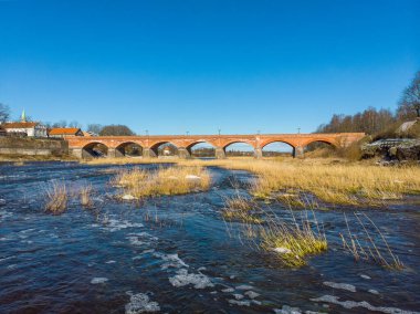 Wenta nehrinin güzel güneşli manzarası eski tarihi Kuldiga kırsalındaki eski tuğla köprüye doğru akıyor. Fotoğraf ılık bir bahar gününde çekildi..