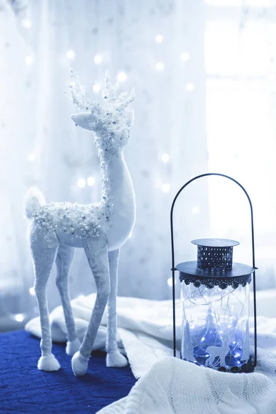 Vánoční dekor bílý jelen s tmavou a skleněnou lucernou a světly na modré a bílé látce v barvě roku 2020 Classic Blue — Stock fotografie