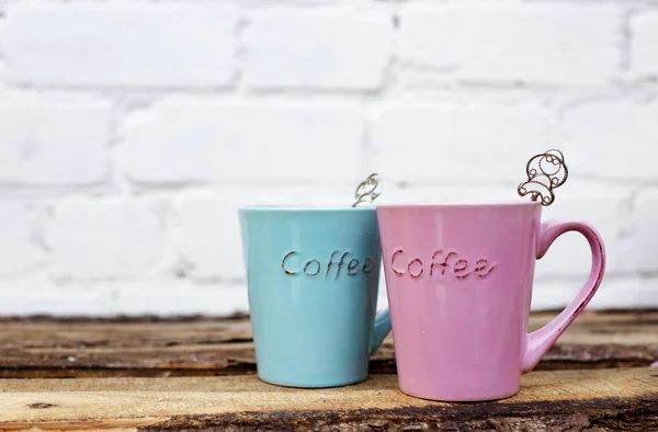 Coloridas copas rosadas y azules para pareja romántica en mesa de madera contra pared de ladrillo blanco para tarjeta de día de San Valentín . — Foto de Stock