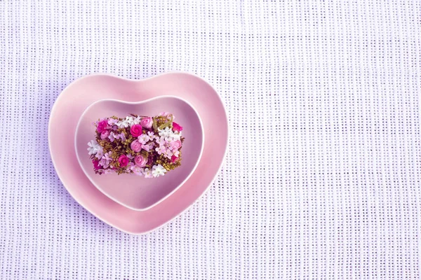 Rosa plater formet som et hjerte med dekorative blomster på hvit tøybakgrunn. Topputsikt. Kjærlighet Valentiner dag flat lå med kopiplass – stockfoto