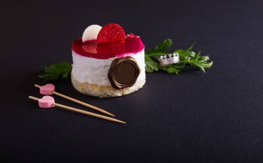 Beyaz sufle ile tatlı bisküvi ve yeşil nane yapraklarının yanında renkli kırmızı çikolata, mücevher taç yüzüğü ve siyah arka planda pembe kalp ile dekoru. Yatay, kapat