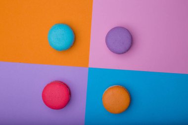Çok renkli kare arka planda tatlı renkli badem kurabiyeleri. Pembe, mavi, turuncu ve mor kurabiyeler. Yatay, üst görünüm