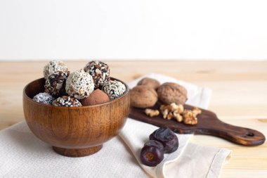 Tahta kasede çiğ protein topları, cevizli ve masada hurma ve beyaz arka planda beyaz peçeteli. Yatay, seçici odak