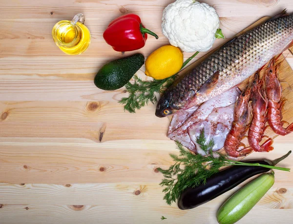 Çiğ beyaz balık, karides, mürekkep balığı, Langoustine ve sebzeli deniz ürünleri tahtası. Zeytinyağı, limon, kabak, biber, karnabahar, avokado ve patlıcan. Üst görünüm, alanı kopyala