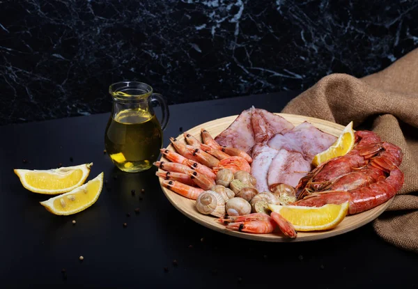 Hafif ahşap tabakta çiğ karides, mürekkep balığı, kabuklu deniz ürünleri ve Langoustines. Siyah arka planda çuval bezli limon ve zeytinyağı. Yatay