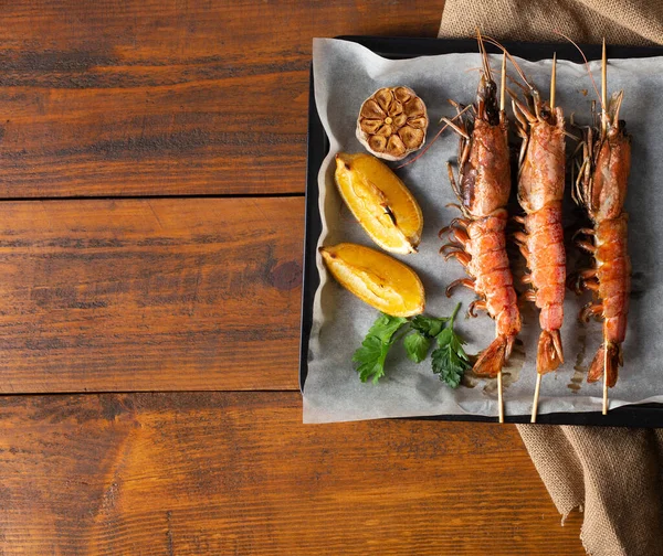 Izgara Langoustine 'li deniz ürünleri panosu, siyah tavada limon ve sarımsak ve ahşap arka planda kağıt torba bezi. Üst görünüm, alanı kopyala