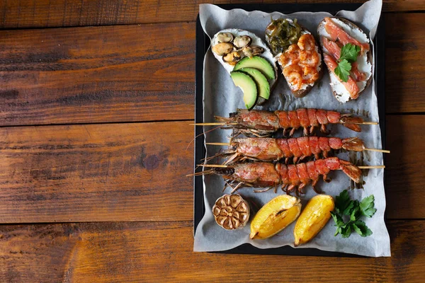 Izgara langoustine, deniz mahsullü sandviçler, ahşap arka planda sarımsak ve limon. Karidesli sandviç, avokado, kırmızı balık, midye ve deniz lahanası. Üst görünüm