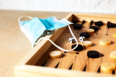 Masa oyunu, ahşap tavla ve arka planda tıbbi maske, karantina sırasında boş zaman kavramı. Kapat.