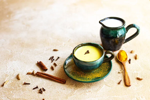 Turmeric golden milk latte with spices. Ceramic jug of milk, wooden spoon with turmeric, cinnamon sticks, clove and cardamom. Detox healthy cozy drink. Copy space,