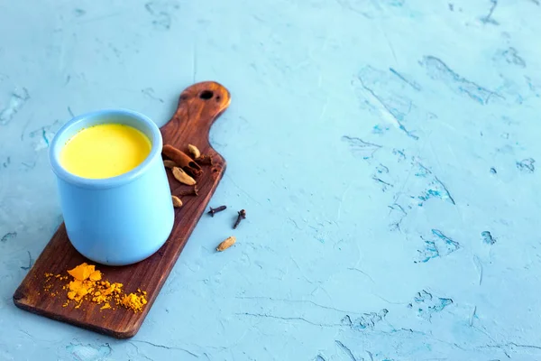 Tahta üzerinde baharatlar olan zerdeçal altın sütlü latte. Mavi arka planda Hindistan içeceği olan seramik kavanoz. Detoks sağlıklı, sıcak bir içecek. Uzayı kopyala, yatay