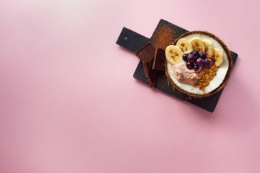 Böğürtlenler, muzlar, kakao ve yoğurttan yapılan lezzetli bir meyve püresi. Çikolatalı hindistan cevizi kasesinde servis edilmiş. Pembe arka planda sağlıklı yaşam, temiz yeme konsepti. Boşluğu kopyala, üst görünüm