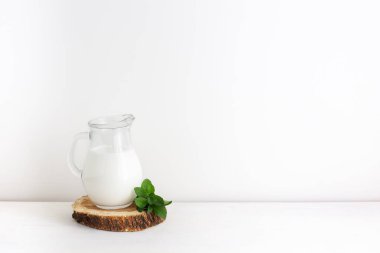 Cam süte mayalanmış süt, beyaz arka planda daire şeklinde ahşap kısımda nane yaprakları. Uzayı kopyala, yatay