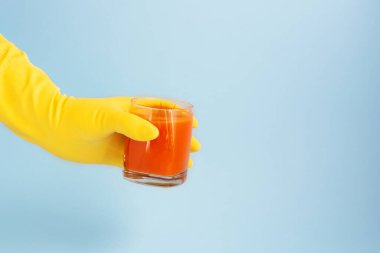 Sarı lateks eldiven ve açık mavi arka planda taze havuç suyu tutan bir el. Koronavirüs karantinası sırasında sağlık koruması. Lastik eldiven. Boşluğu kopyala