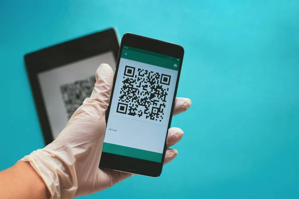 Coronavirus karantinası sırasında QR kodu taranıyor. Mavi arka planda doğrulama için lateks eldiven, cep telefonu taraması QR kodu kullanın. COVID-19 kontrol. Lastik eldiven. Boşluğu kopyala.