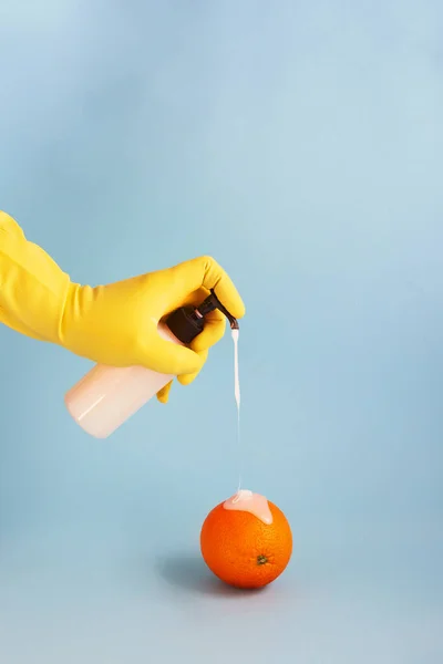 Sarı lateks eldivenler, mavi gri arka planda turuncu üzerine dezenfektan tutuyorlar. Coronavirus karantinası sırasında tropikal meyveli sıvı sabun akışı. Lastik eldiven. Dikey, boşluğu kopyala