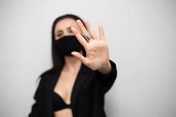 Ameliyat maskesi takan genç seksi bir kadının stüdyo portresi ve gri arka planda uzanan siyah bir iç çamaşırı. Grip ve koronavirüs salgını, toz alerjisi, virüse karşı koruma. Güzel bir sosyal mesafe konsepti. Dur işareti, yerli.