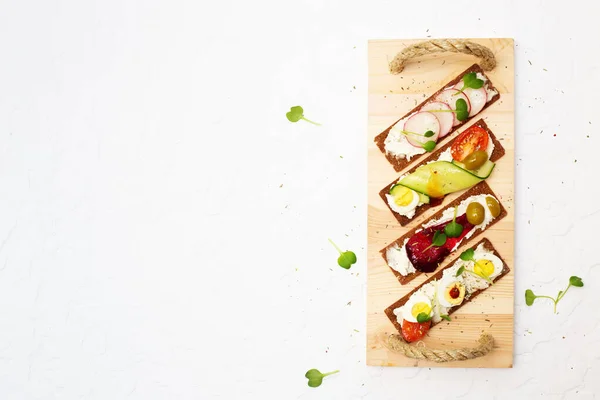 Cips, krem peynir, sebze ve tereyağlı ahşap tepside mikroyeşil sandviçler. Salatalık, domates, bıldırcın yumurtası, turp, havuç, pancar, zeytin ve beyaz arkaplanda mikro yeşillikler. Mikro yeşil daikon filizleri. Merhaba.