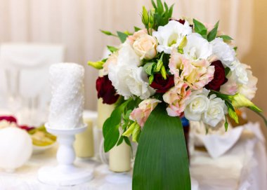 Restorandaki şenlikli bir düğün masasında çiçek buketleri. Beyaz, kırmızı ve gül çiçekli bir mum. Yatay