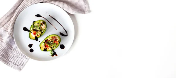 Avokado kasesine salatalı sağlıklı vejetaryen yemeği. Avokado, domates, balzamik soslu mikroçerez beyaz tabakta vejetaryen aperatifi ve beyaz arka planda gri peçete. Üst görünüm, alanı kopyala.