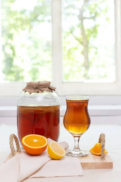 Farklı aromalı ev yapımı mayalanmış çiğ kombu çayı. Sağlıklı, probiyotik aromalı, cam kavanozda mantarlı ve pencerenin yanındaki camda bulunan bir içecek. Tarçın ve turunçgiller