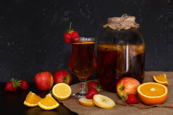 Farklı meyve aromalı ev yapımı mayalanmış çiğ kombu çayı. Sağlıklı, probiyotik aromalı, mantarlı cam kavanozlu ve koyu arkaplanlı bir cam. Tarçın, narenciye, çilek