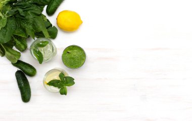 Beyaz arka planda sağlıklı beslenme ve kilo kaybı için yeşil ıspanaklı smoothie ve salatalık ve limonla detoks suyu harmanlanmış. Yaz sebzeli ve malzemeli sağlıklı içecek. Üst görünüm, alanı kopyala
