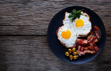 Yağda yumurta, domuz pastırması ve ahşap tabakta siyah bir arka plan..