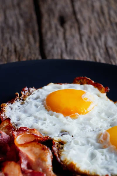 Huevos fritos con tocino en un plato de madera sobre fondo negro . — Foto de Stock