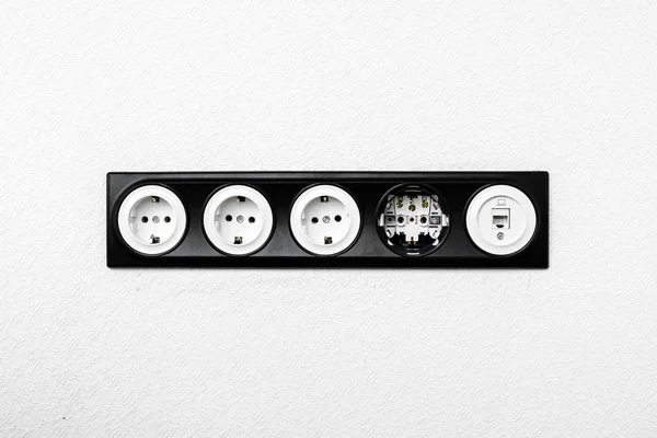 five black white sockets in the white wall