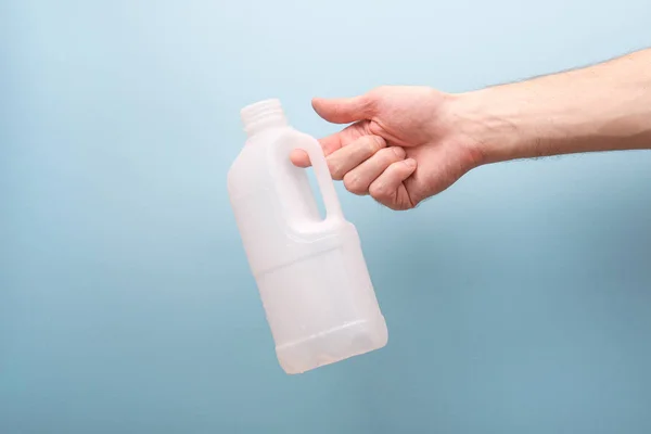 Empty bottle of milk in male hands on a light blue background. Plastic milk canister on a blue background with place for text.
