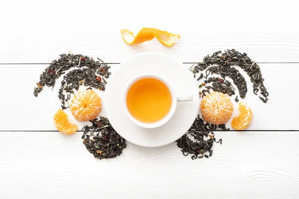 A cup of fruit tea on white boards with tangerines. View from above. Composition with a cup of herbal tea on a light background.
