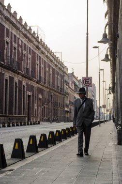 Takım elbise giymiş yetişkin bir adam Mexico City şehir merkezinde bir pazar sabahı boş bir sokakta yürür.