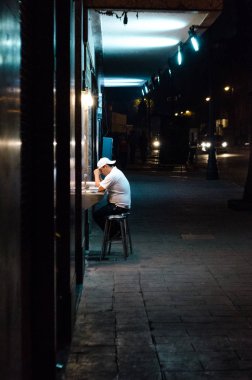 Geceleri açık bir dükkanın önündeki bankta oturan endişeli bir adam.