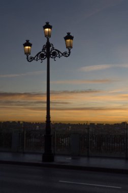 Sıcak renklerle dolu bir günbatımında sokak lambaları açık olan eski bir sokak lambası.