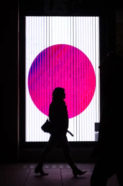 Silhouette of a woman walking in profile to a spectacular pink advertisement