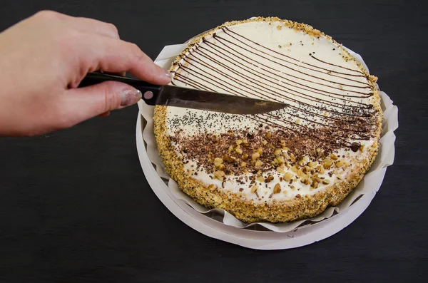 hand cuts a cake with a knife. Tasty cake with condensed milk and poppy seeds on a black table.
