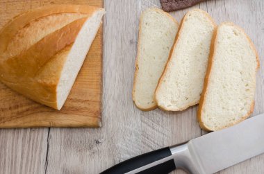 Tahta ve bıçağın üzerinde uzun bir somun ekmek. Lezzetli Ukrayna ekmeği. Dilimlenmiş beyaz ekmek.