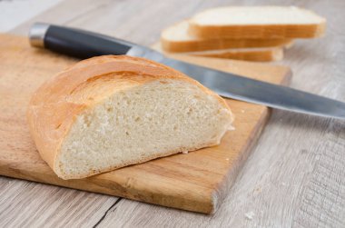 Tahta ve bıçağın üzerinde uzun bir somun ekmek. Lezzetli Ukrayna ekmeği. Dilimlenmiş beyaz ekmek.