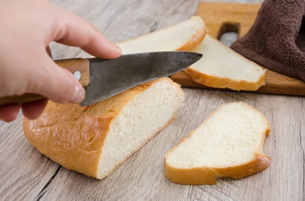 long loaf on a wooden board and knife. Delicious Ukrainian bread. Hand cuts a knife with white bread, close-up ..