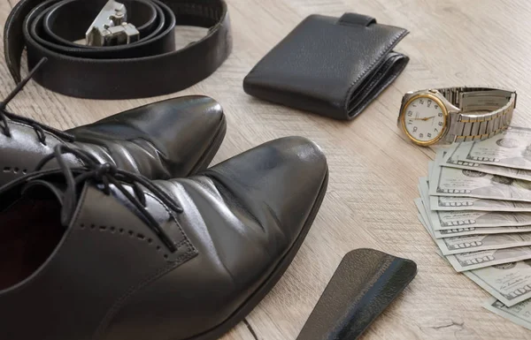 black men\'s shoes with accessories for care. Shoes, dollars, belt, wallet and wristwatch on a wooden background.