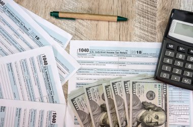 vergi formları 1040, hesap makinesi, dolar ve kalem masada.