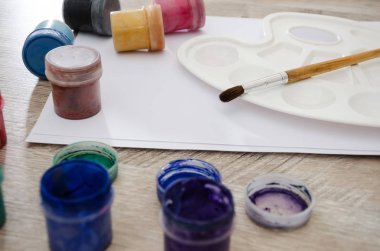 Kavanozlarda renkli guaj, bir fırça ve ahşap bir masaya çizim yapmak için bir palet..