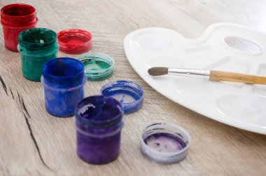 Kavanozlarda renkli guaj, bir fırça ve ahşap bir masaya çizim yapmak için bir palet..