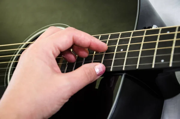 Hand plays the black guitar. Part of an acoustic guitar. Close-up.