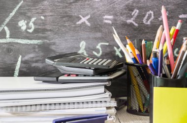 Defterler, defterler, kalemler, hesap makineleri ve yazı araçları. Örneklerle dolu bir karatahtaya karşı. Eğitim kavramı.