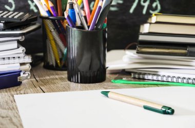 Defterler, defterler, kalemler, hesap makineleri ve yazı araçları. Örneklerle dolu bir karatahtaya karşı. Eğitim kavramı.