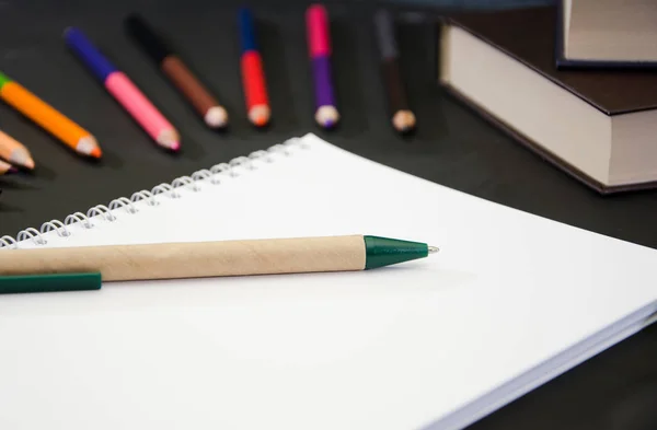 Koncepcja Edukacji Notatnik Długopisem Tle Kolorowych Ołówków Książek Czarnym Stole — Zdjęcie stockowe